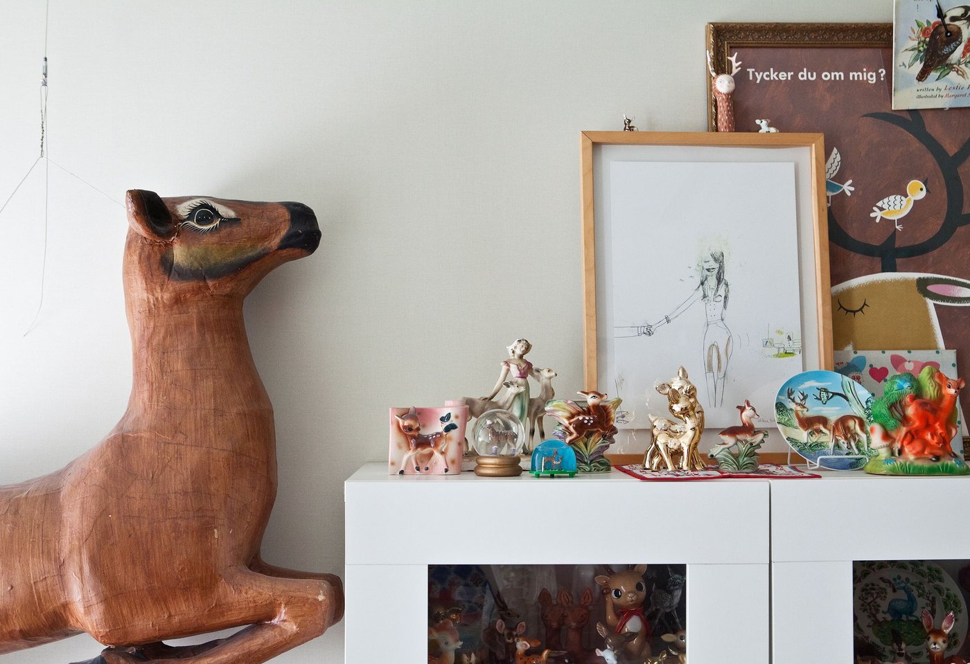 A collection of deer toys and figurines are displayed inside and above a white closet, while a big toy statue of a deer hangs beside it.