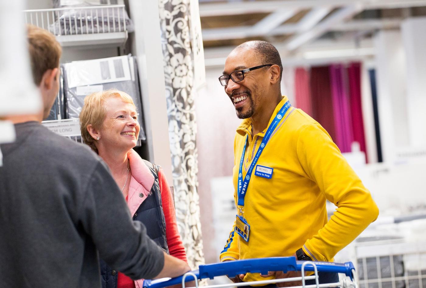 An IKEA co-worker wearing a yellow shirt talks with customers inside an IKEA store.