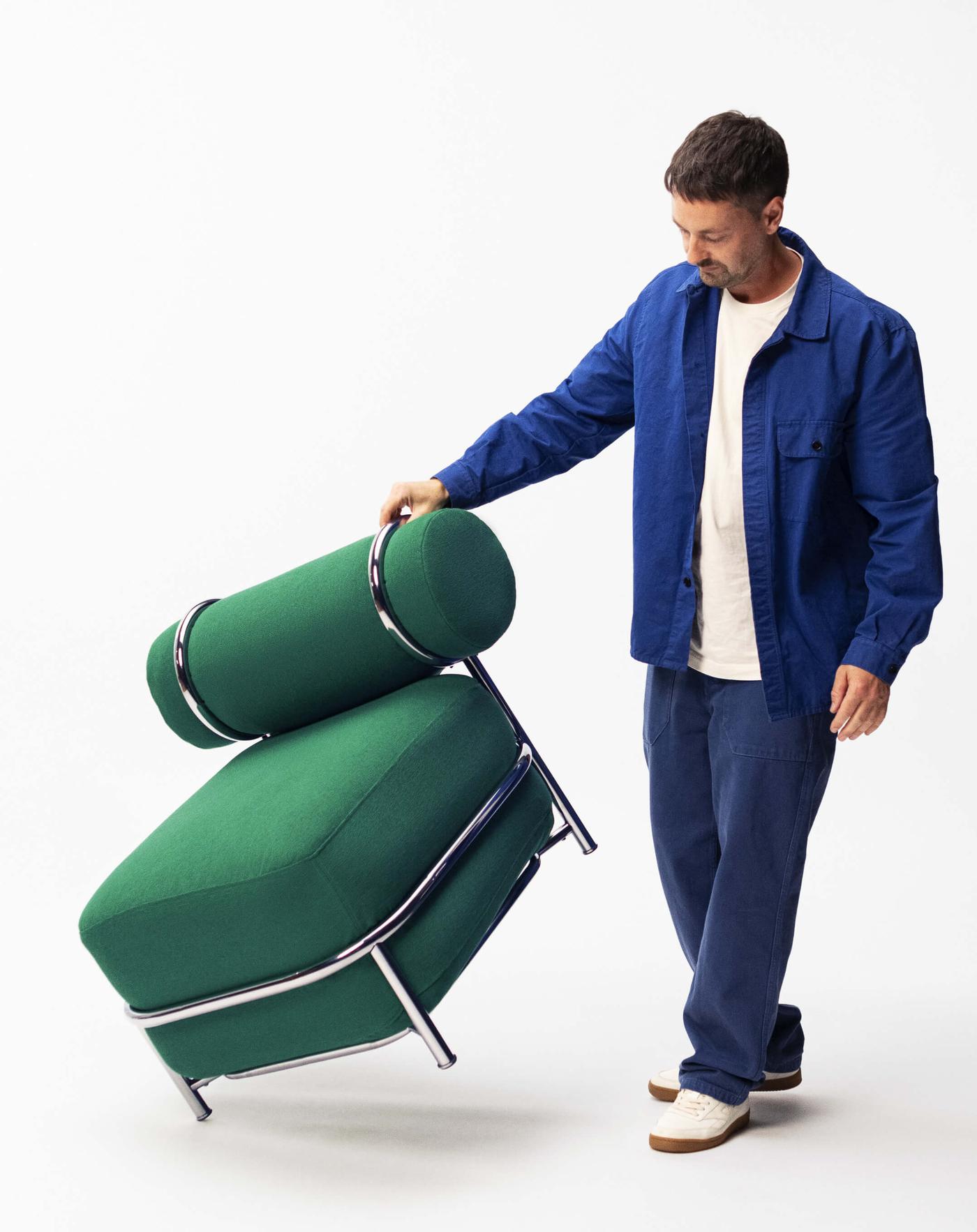 IKEA designer Mikael Axelsson lifts up a green IKEA PS 2026 chair on one side.
