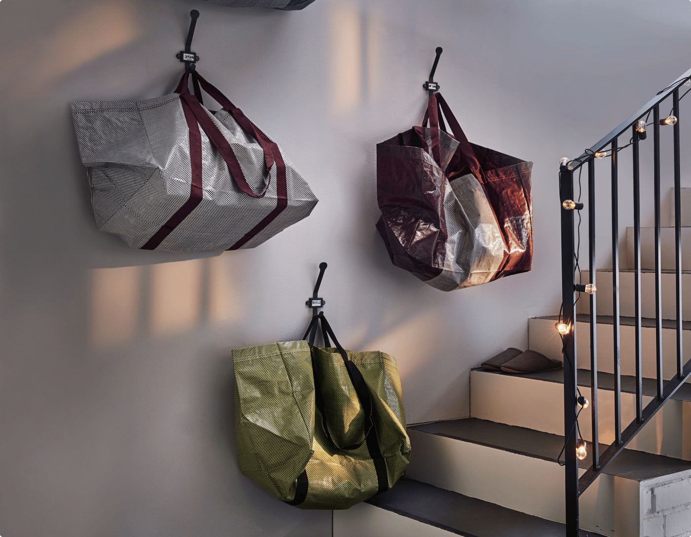 Three YPPERLIG carrier bags in different colours hang on a wall next to a staircase.
