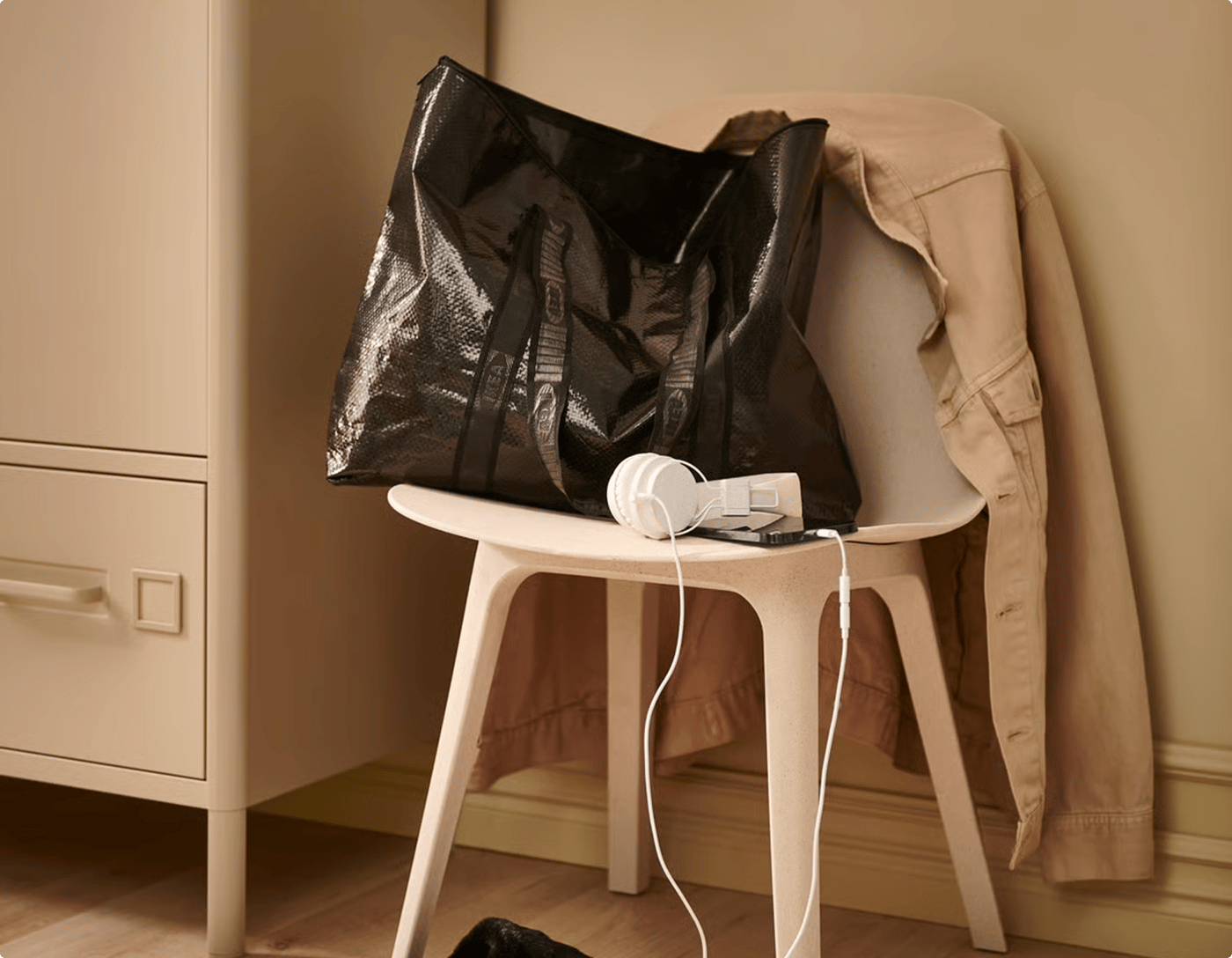 A black bag is placed on a chair, next to a pair of headphones in a beige room setting