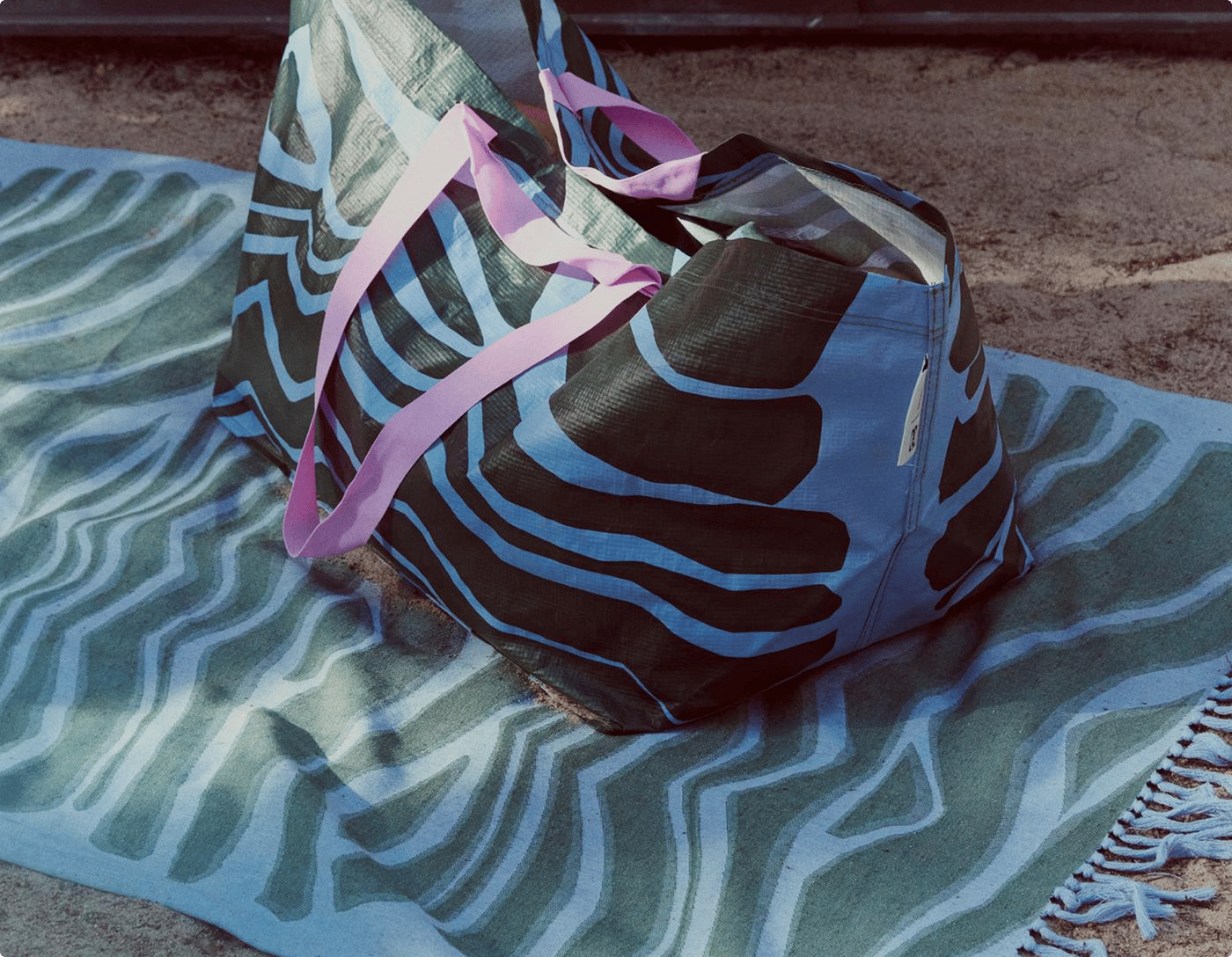 A green and blue patterned bag is placed on a matching patterned beach towel.