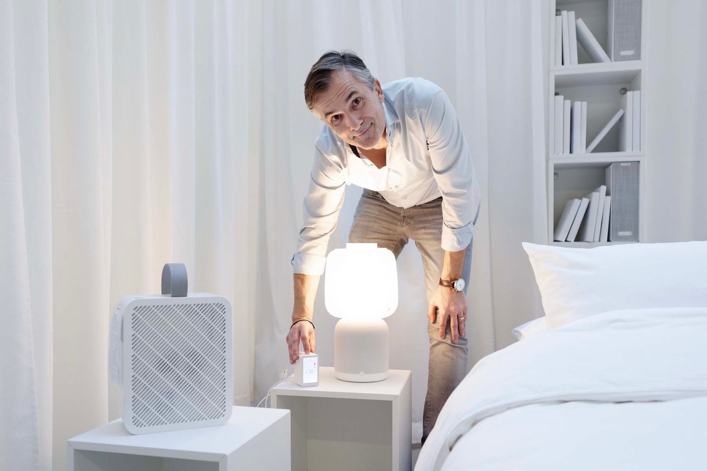 IKEA product design developer Stjepan Begic stands over a SYMFONISK speaker lamp, an air purifier, and an air quality sensor.