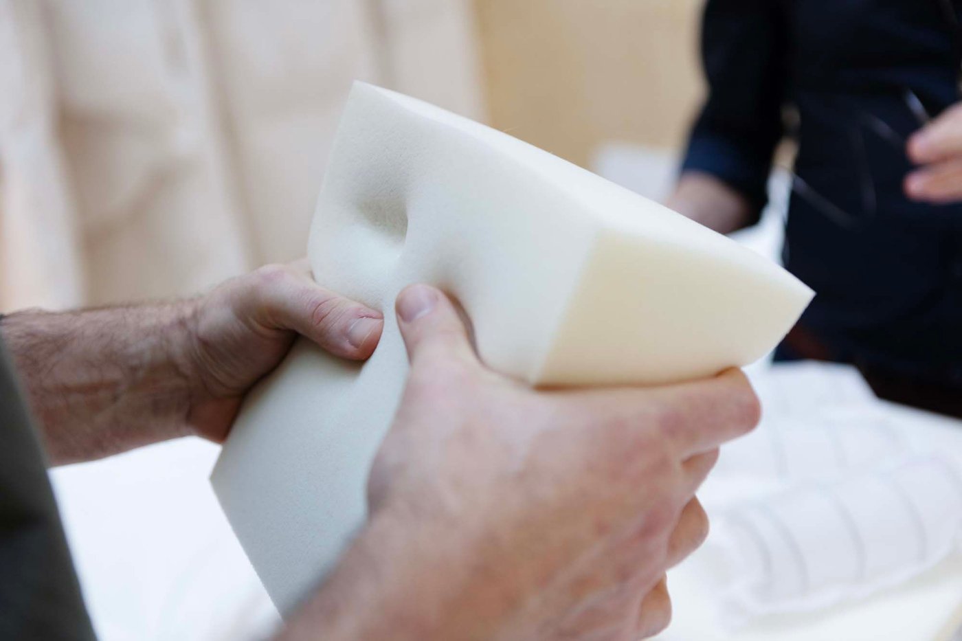 A pair of hands squash a square of mattress foam.