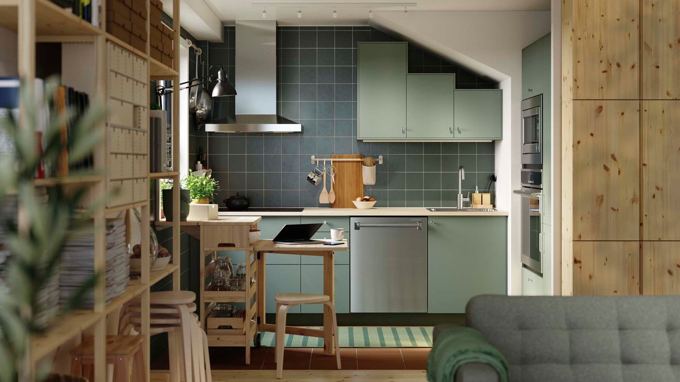 A kitchen space featuring green cabinets and a mobile drop-leaf table with storage.