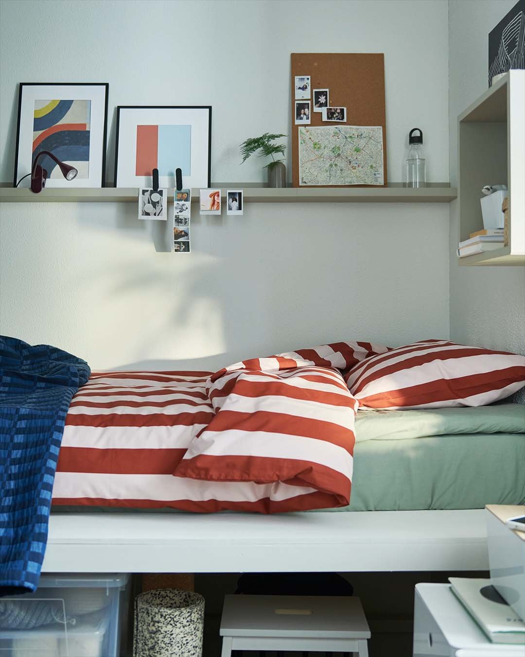 Corner of a bedroom with a playfully-styled single bed and shelf with art.