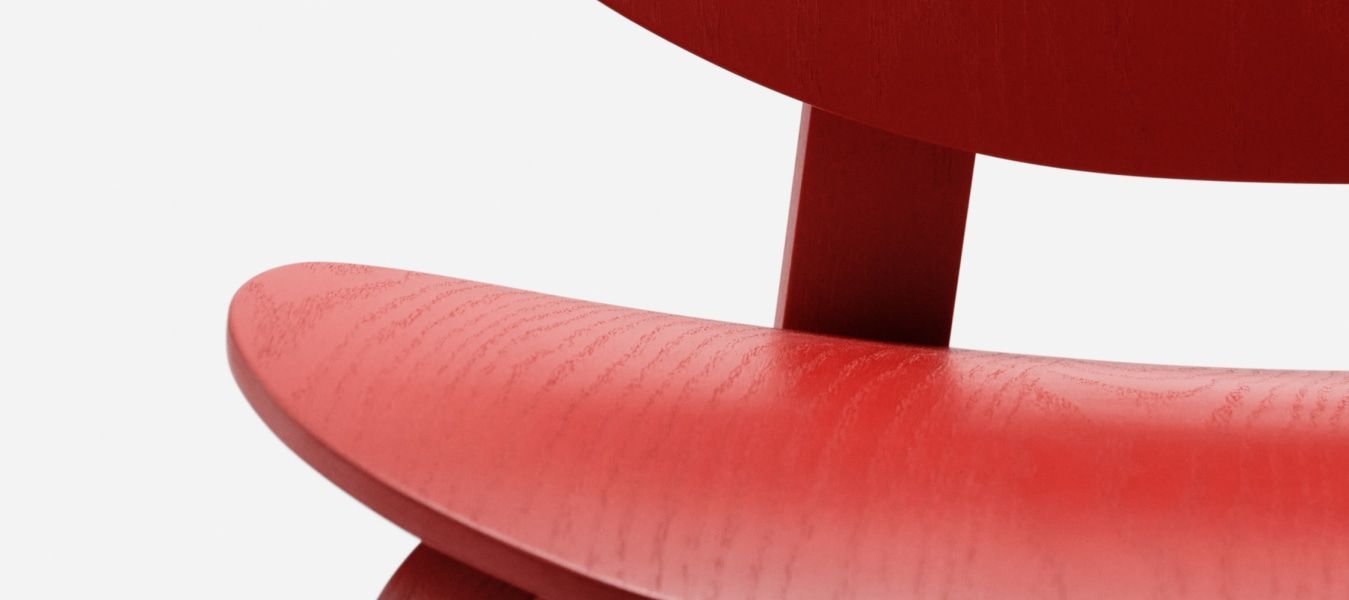 A detail shot of a red wood chair. The seat is curved.