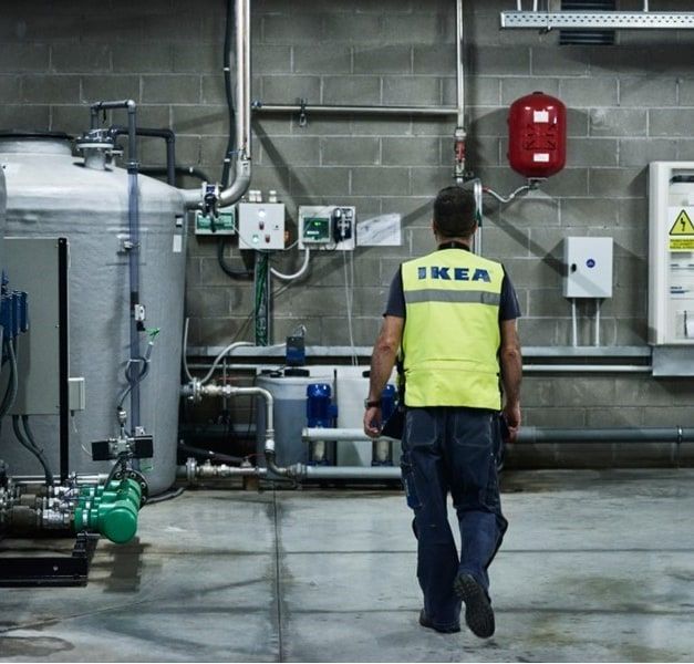 A factory environment in grey cement with two large containers on the left and an IKEA co-worker with a neon-yellow vest.