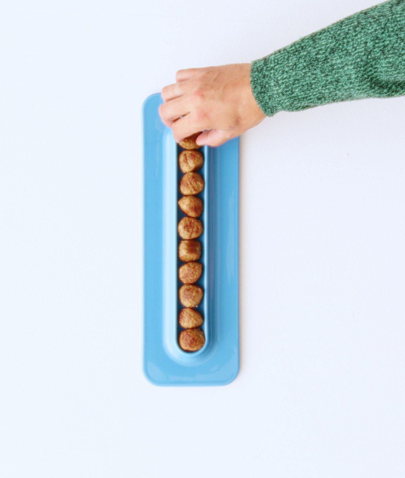 A hand reaches across to grab a meatball from a special blue ceramic serving plate that has a channel down the middle that holds a single line of meatballs.