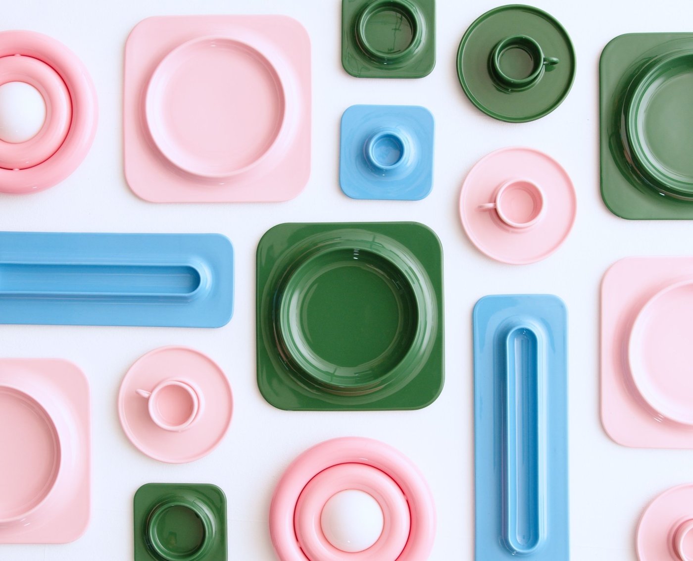 A collection of ceramic tableware with rounded shapes and bright colours such as pink, green and sky blue are shown from a top-down angle.