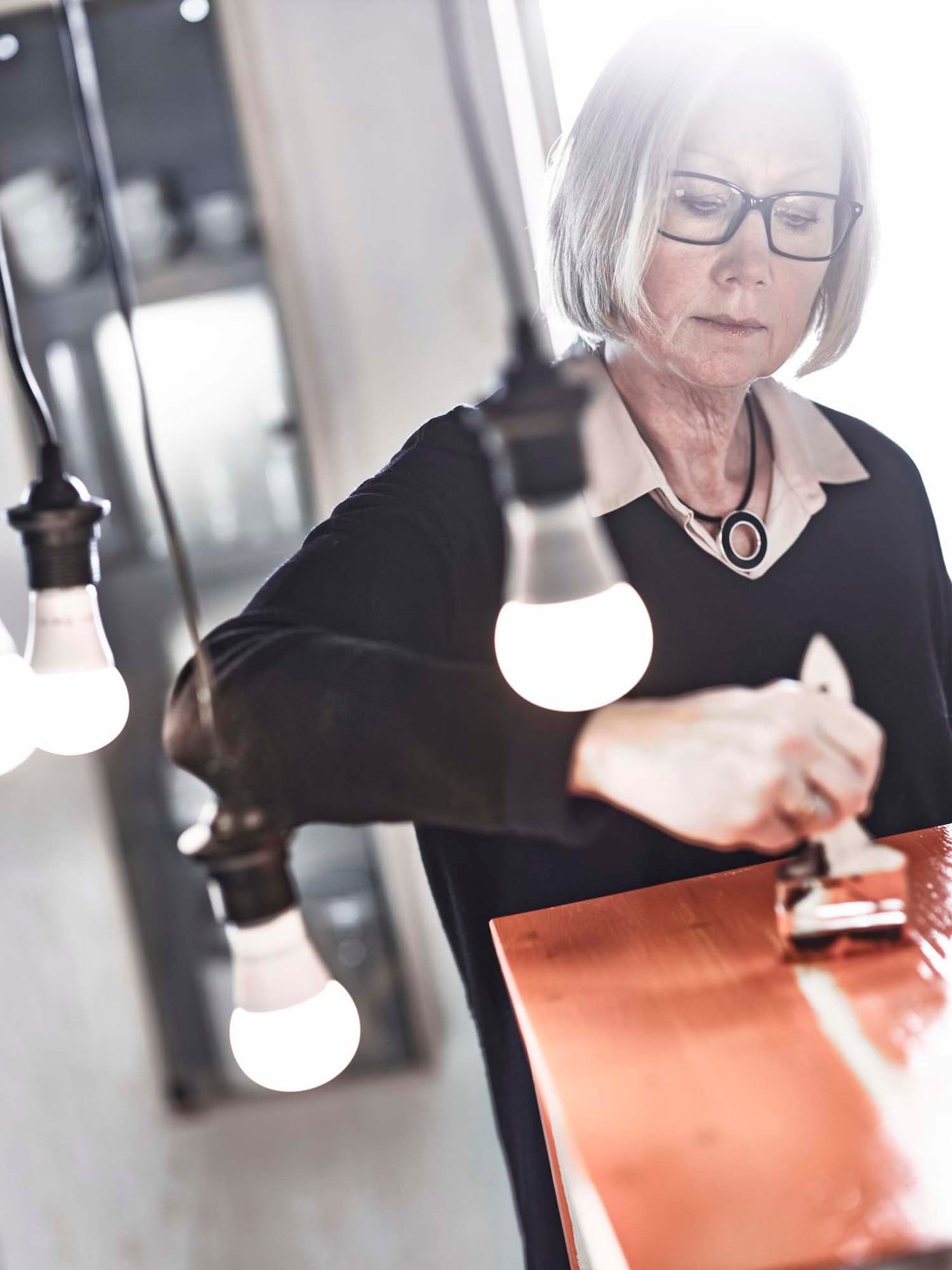 Marianne Hagberg painting. There are lightbulbs hanging in front of her.
