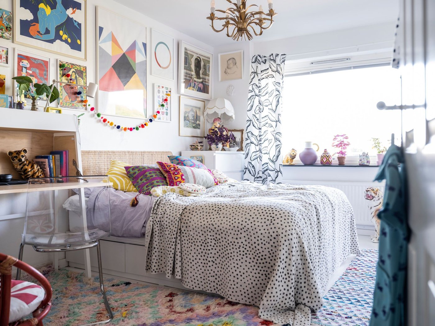 A white bedroom, decorated with photos and ornaments. The bed has cushions.