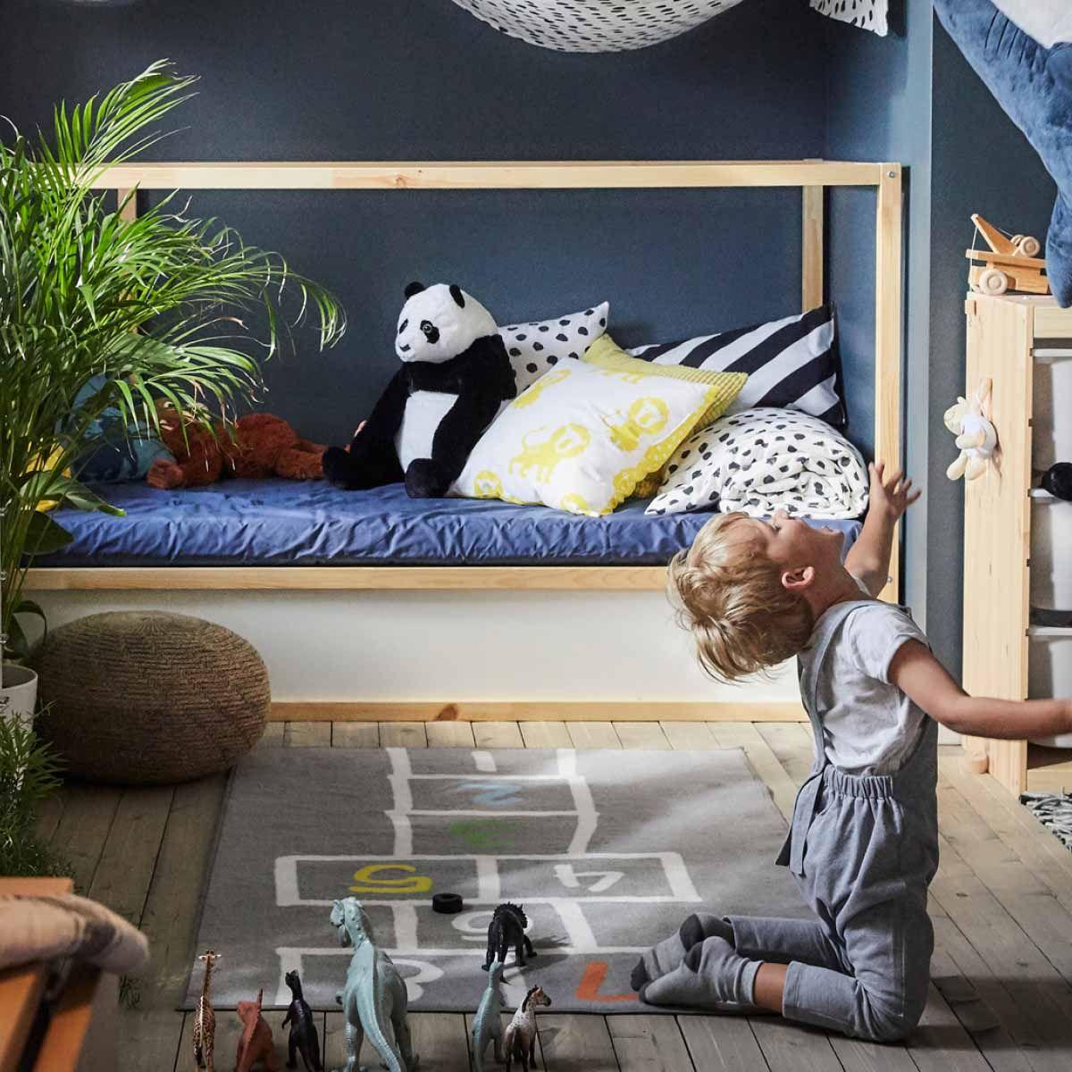 A child playing on the floor of a bedroom, throwing a soft toy into the air.