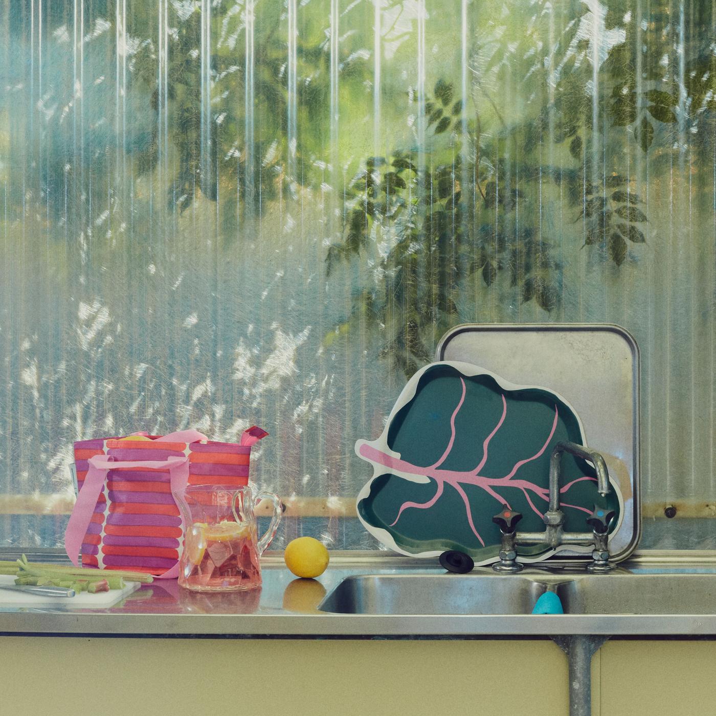 A leaf shaped tray standing on a kitchen top together with a jug, a bag and a lemon.