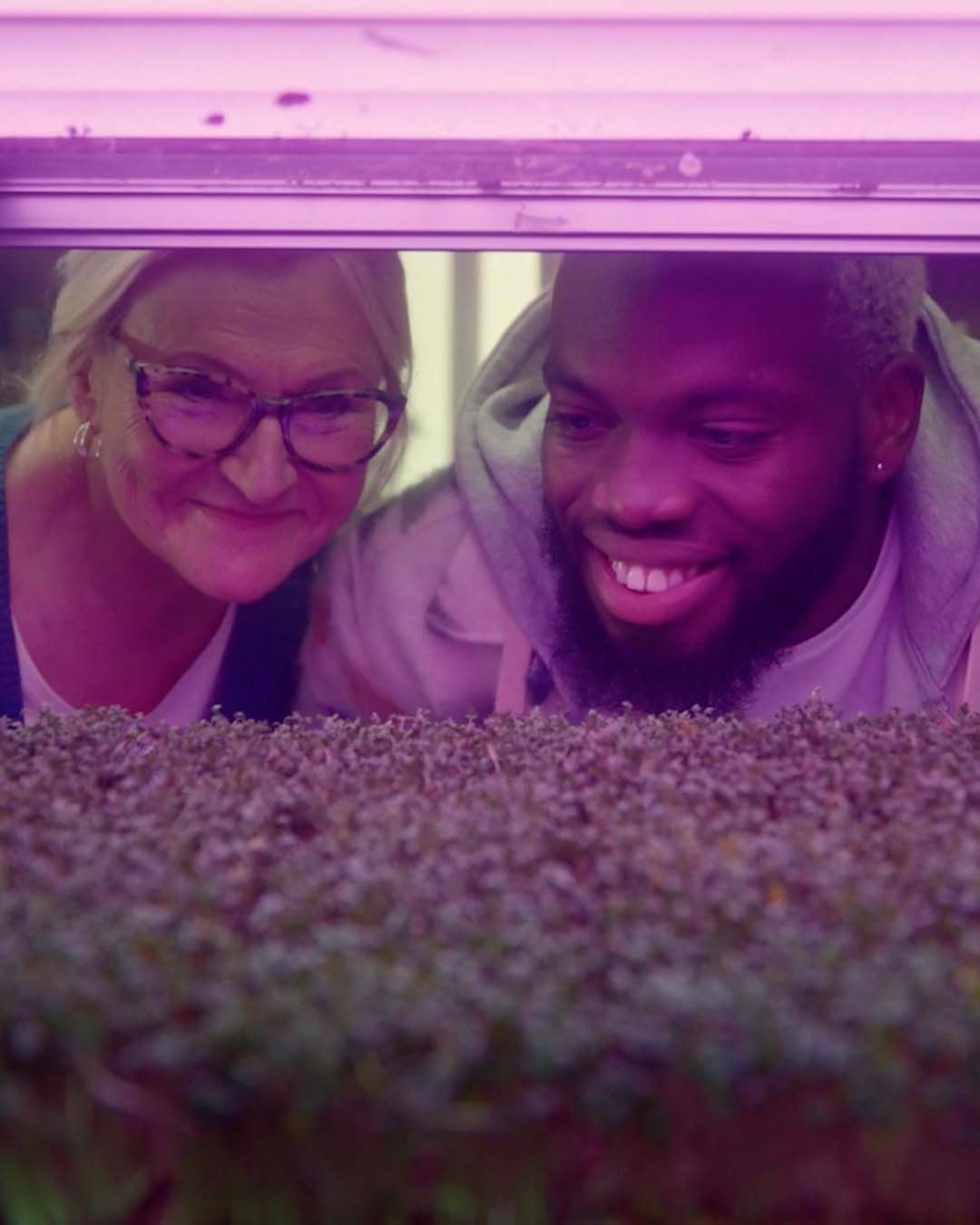 A man and woman look at seedlings under UV light. They are smiling.
