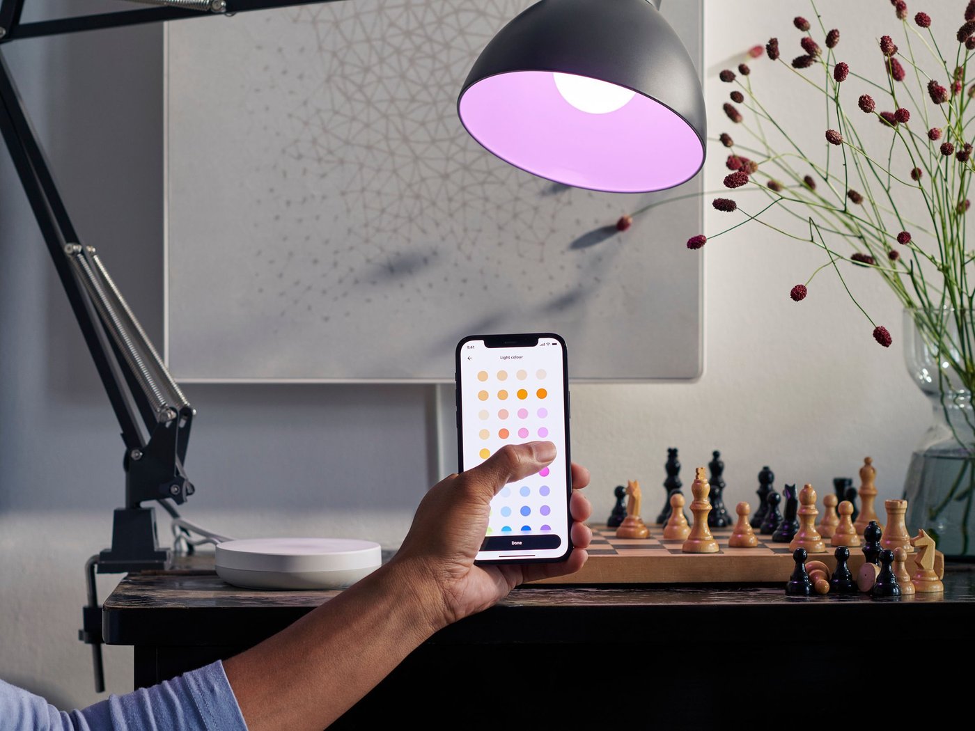 A hand holding a smartphone in front of a lamp.