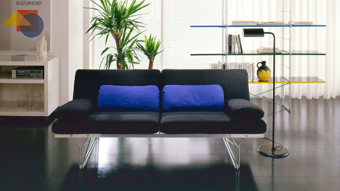 Modern IKEA living room from the 1980s with a black sofa with bright blue backrest cushions.