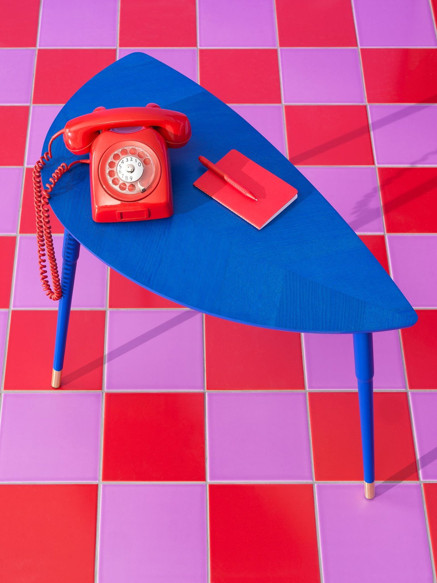 A blue table shaped like a leaf, with a red telephone and a red notebook on it.