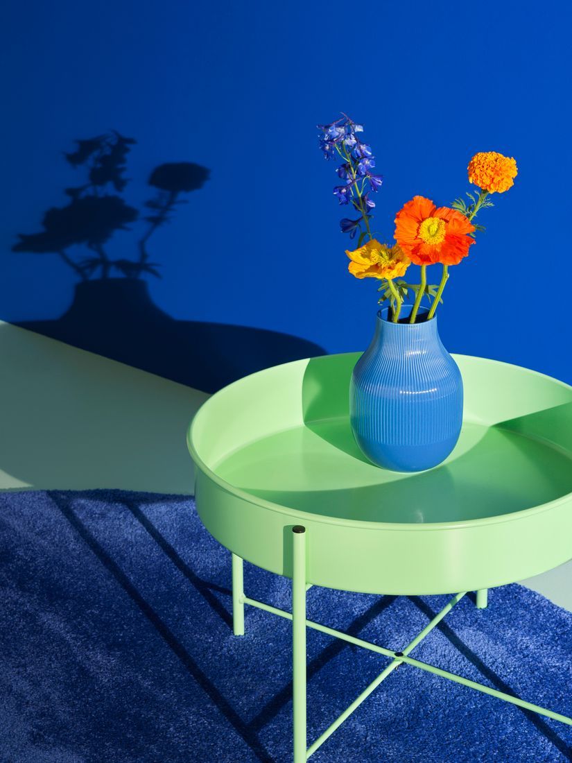 A green table with a blue vase standing in a room with a blue wall. 