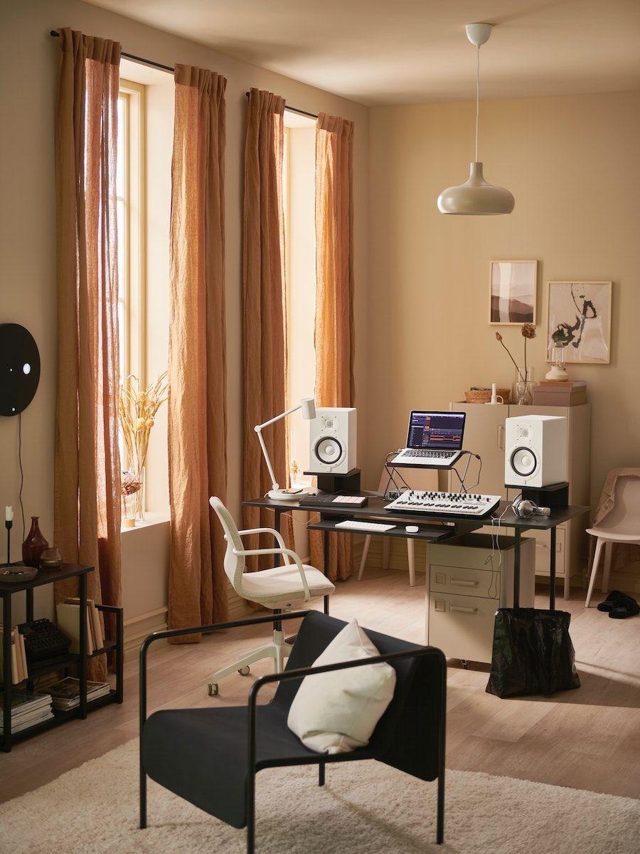 A living room with a black desk whit a computer, a mixer and two speakers on it.