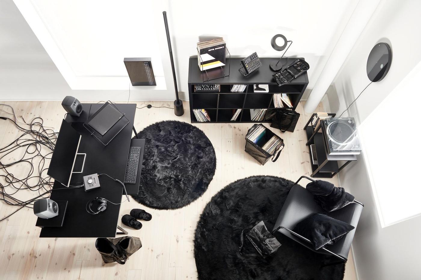 A room furnished with a black desk, a black KALLAX shelf, black carpets, and a black chair.