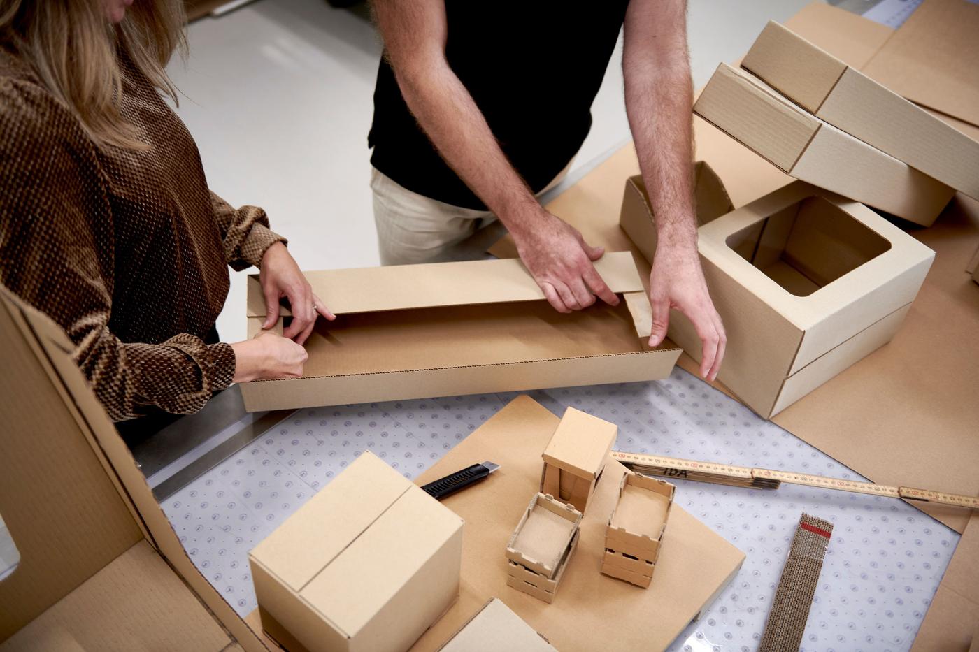 Two people assembling cardboard packaging on a work surface.