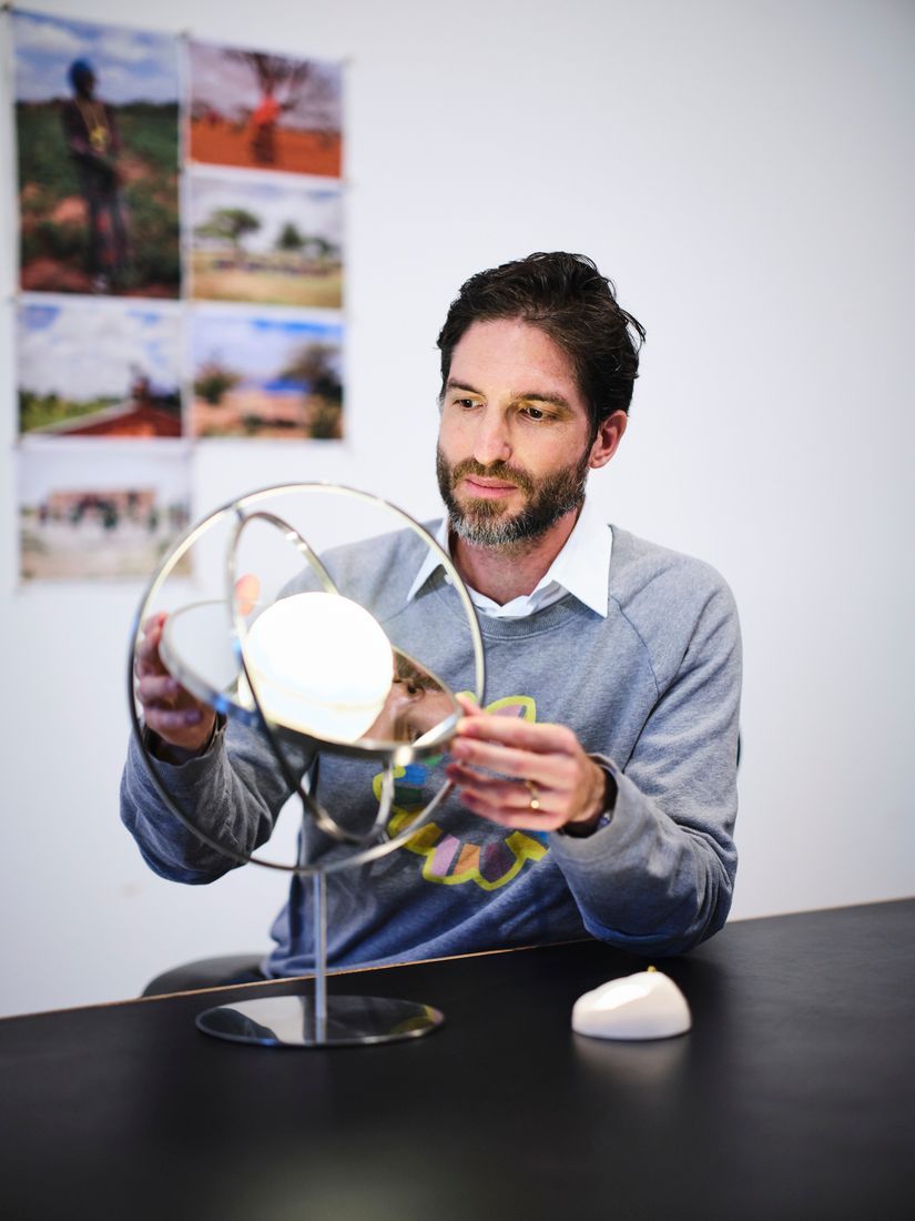 A man in a grey shirt sitting at a desk holding his hands on a stainless solar powered lamp.