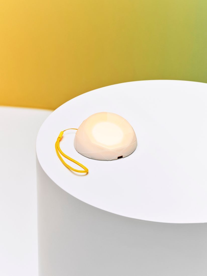 A white solar powered lamp with a yellow string attached to it lying on a white surface.