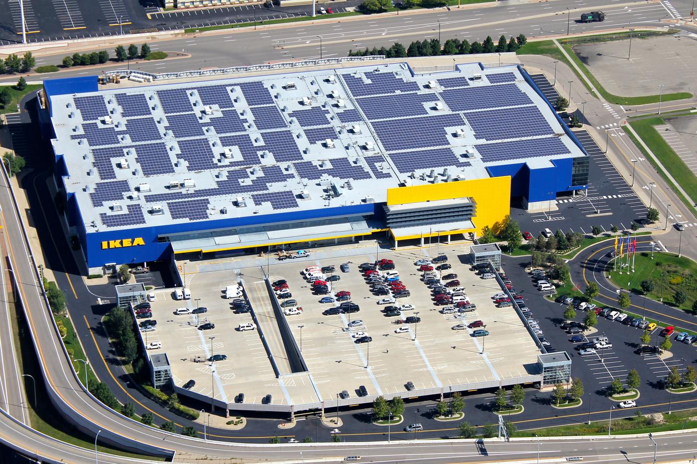 An entire IKEA store on a sunny day. The parking lot hosts a few cars and the store roof is covered by solar panels.