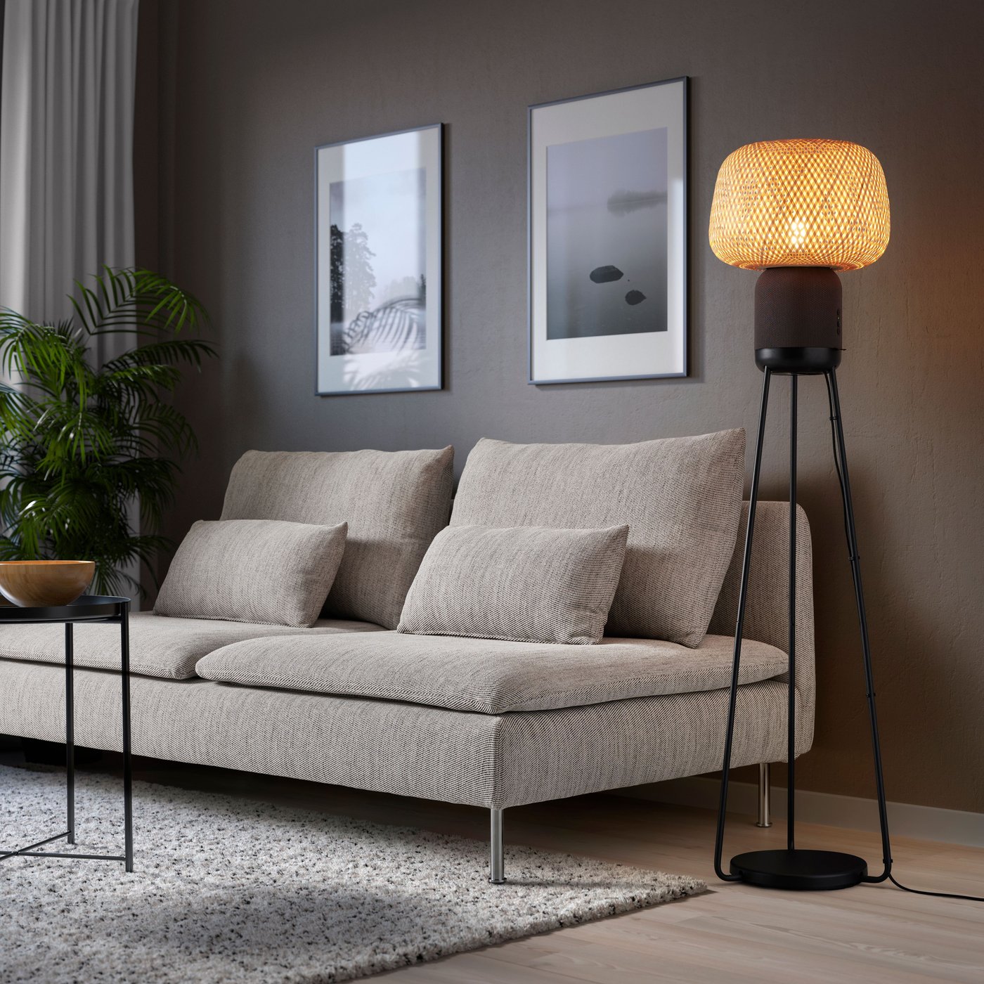 A lamp speaker standing on a tripod, next to a sofa. 