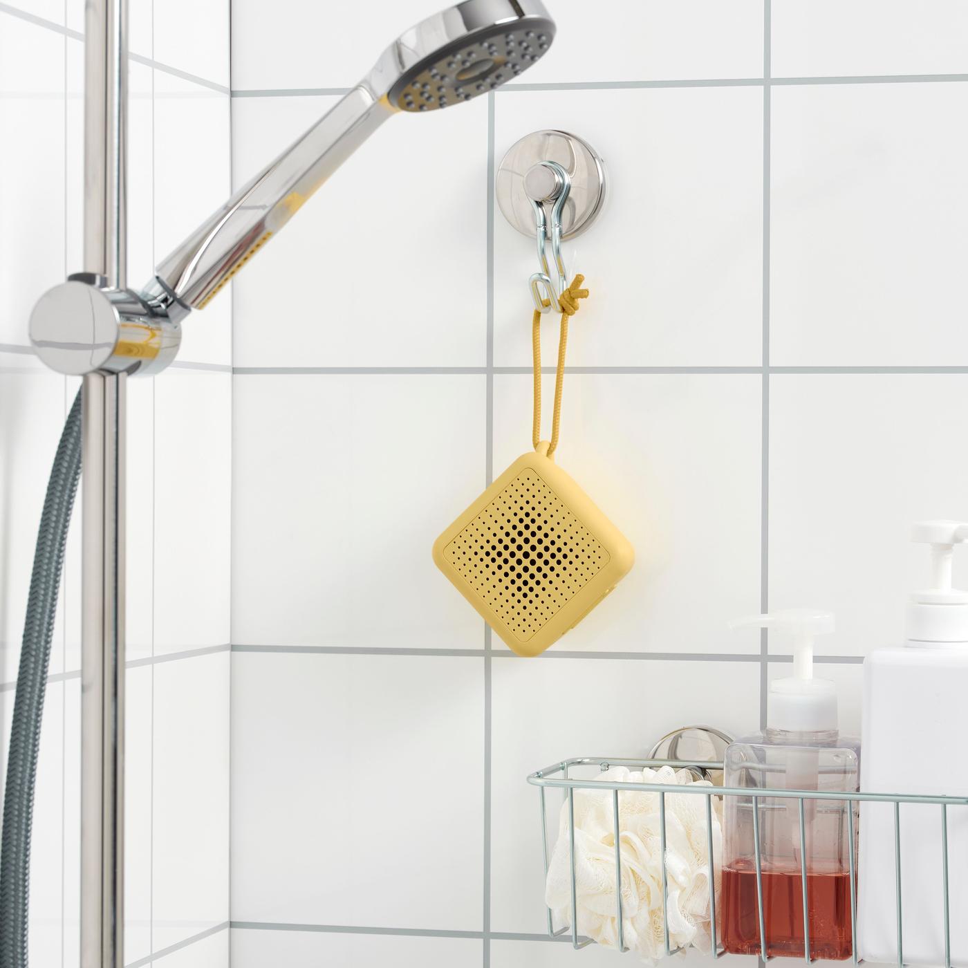A yellow Bluetooth speaker hanging on a hook in a white tiled shower.