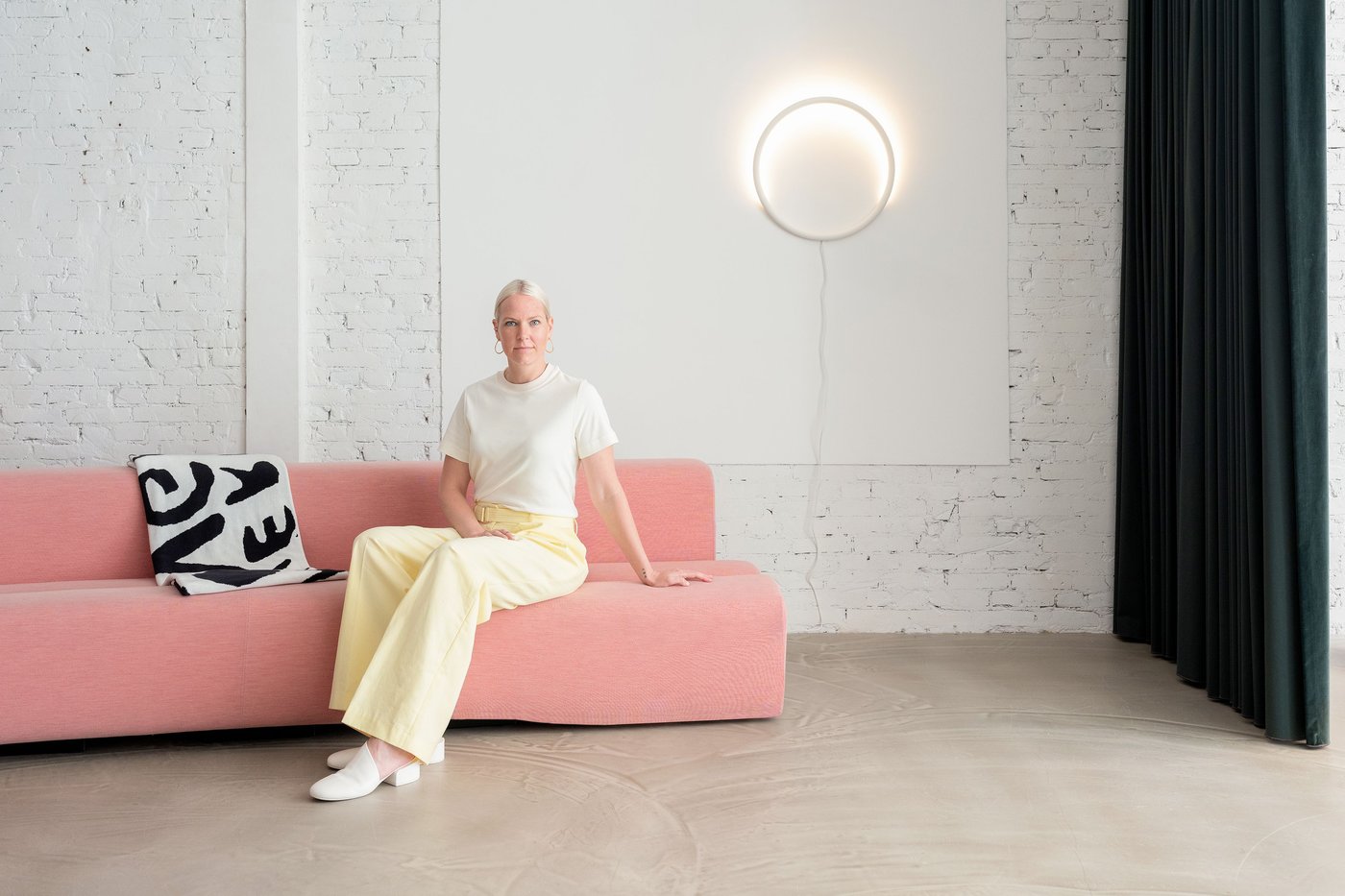A woman in yellow pants and white shirt sitting in a pink sofa.