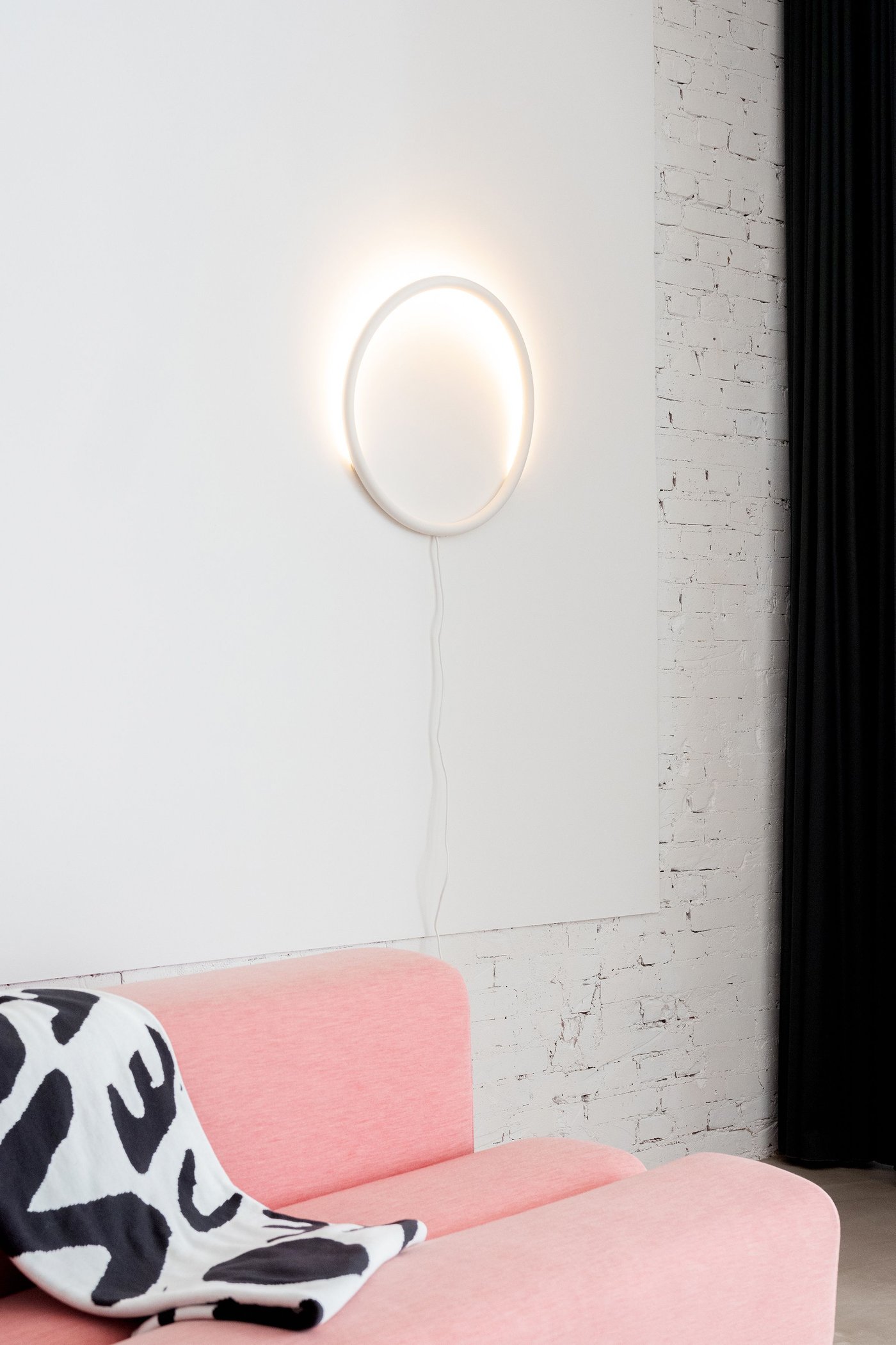 A lamp hanging on a wall behind a pink sofa.