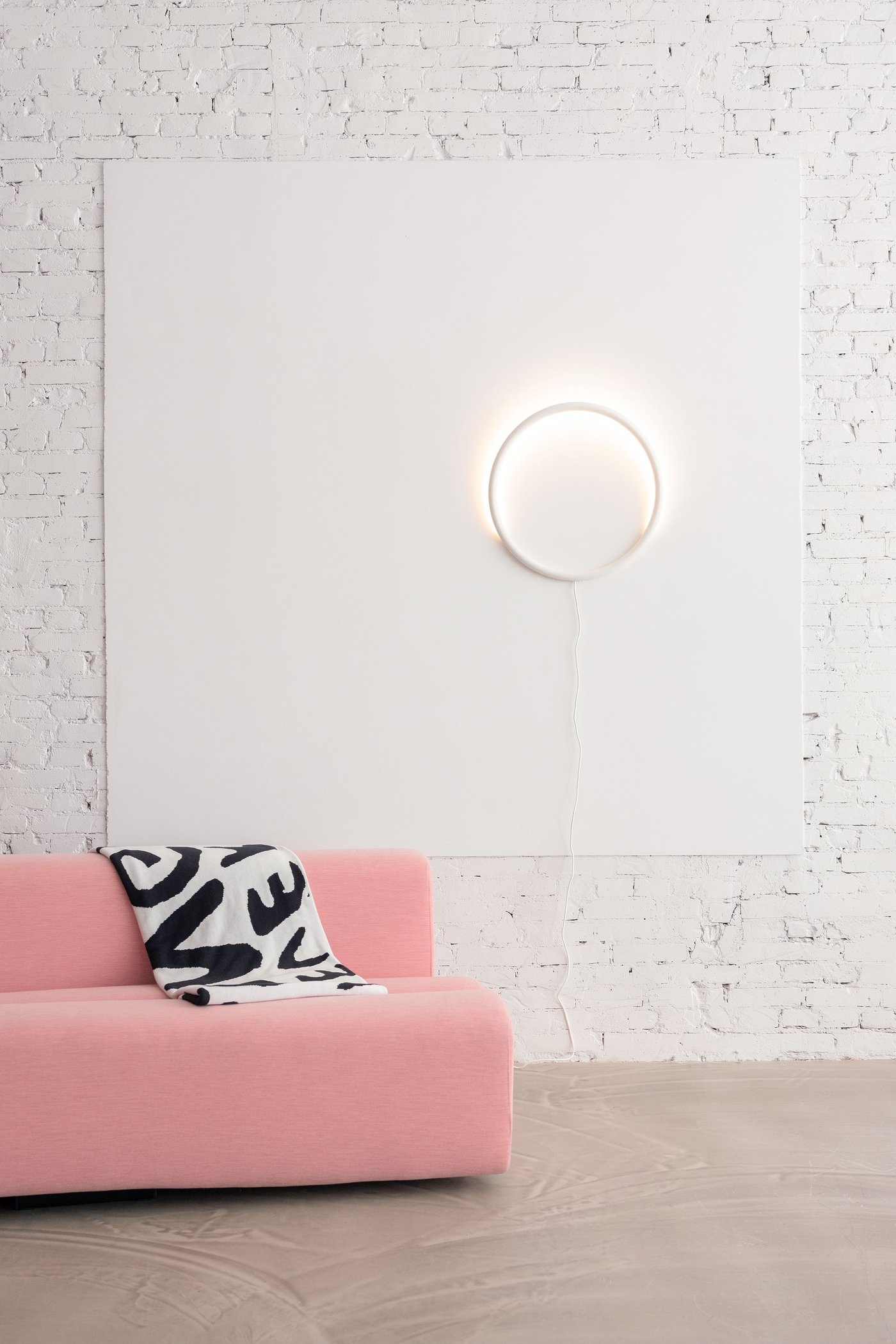 A pink sofa in a white room with a circular lamp on the wall.