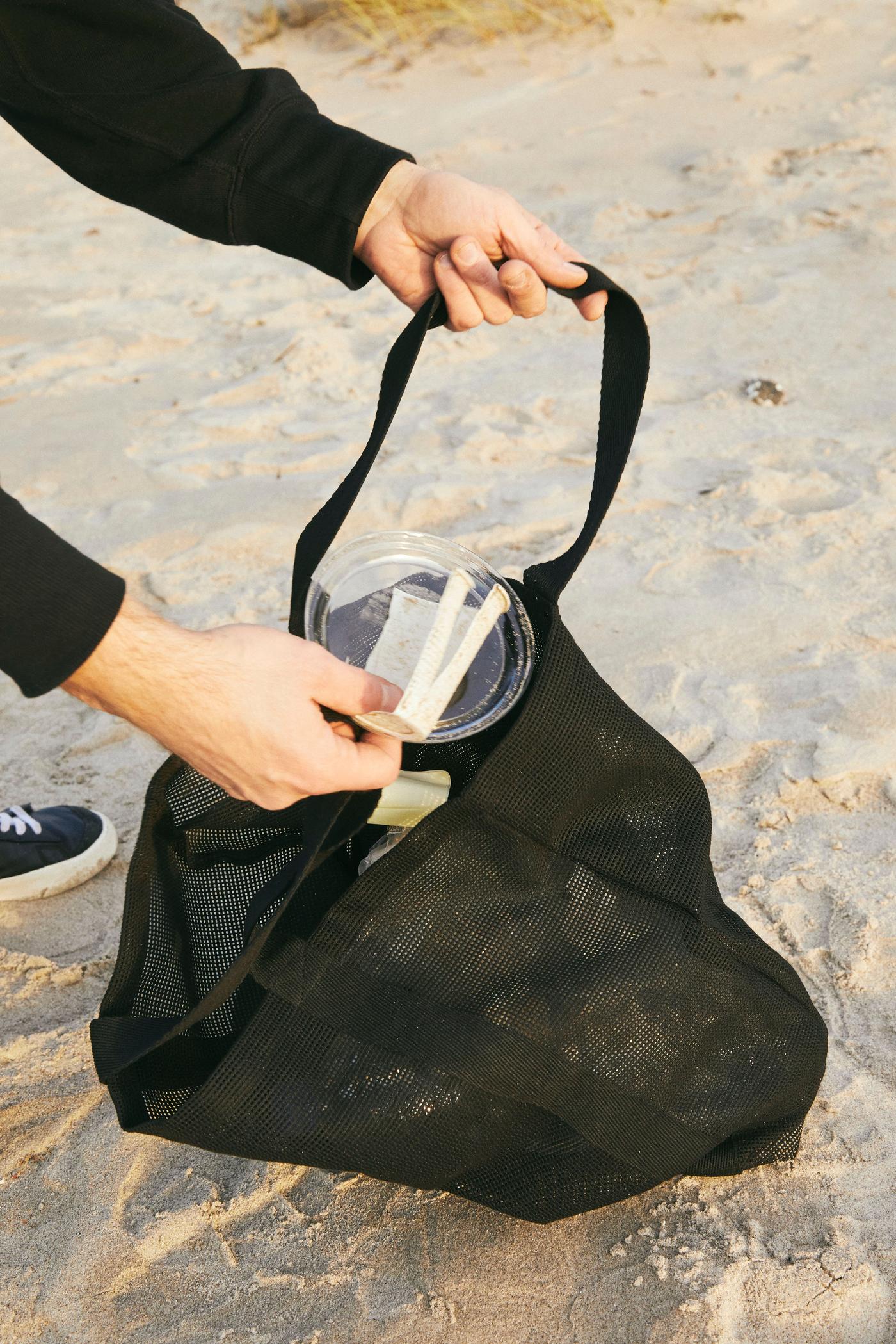 Two hands holding a black bag on the beach.