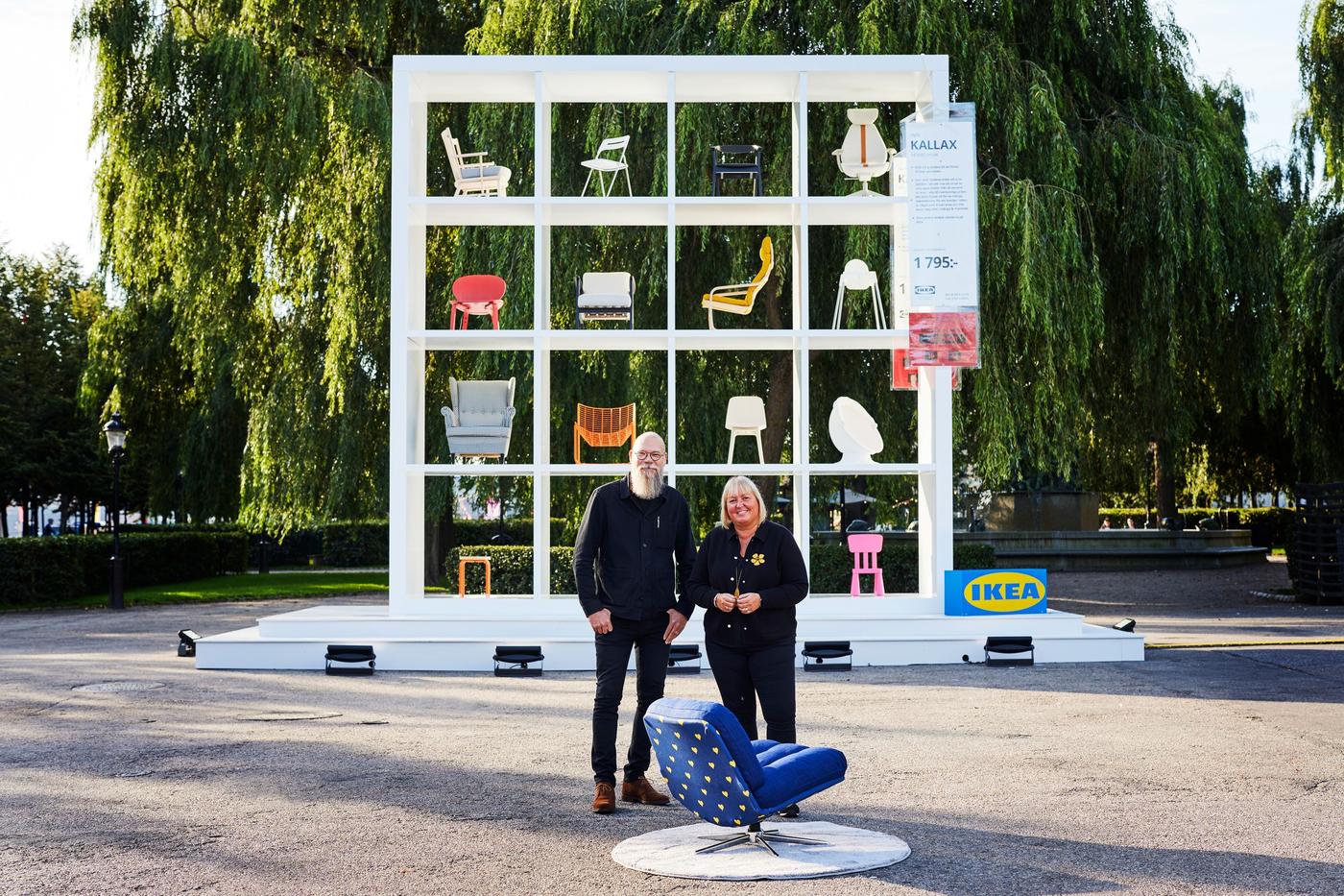Johan Ejdemo and Emily Birkin stand in front of a large display of IKEA furniture in Stockholm. They are standing behind a specially designed armchair created to celebrate the King of Sweden's 50th year on the throne.