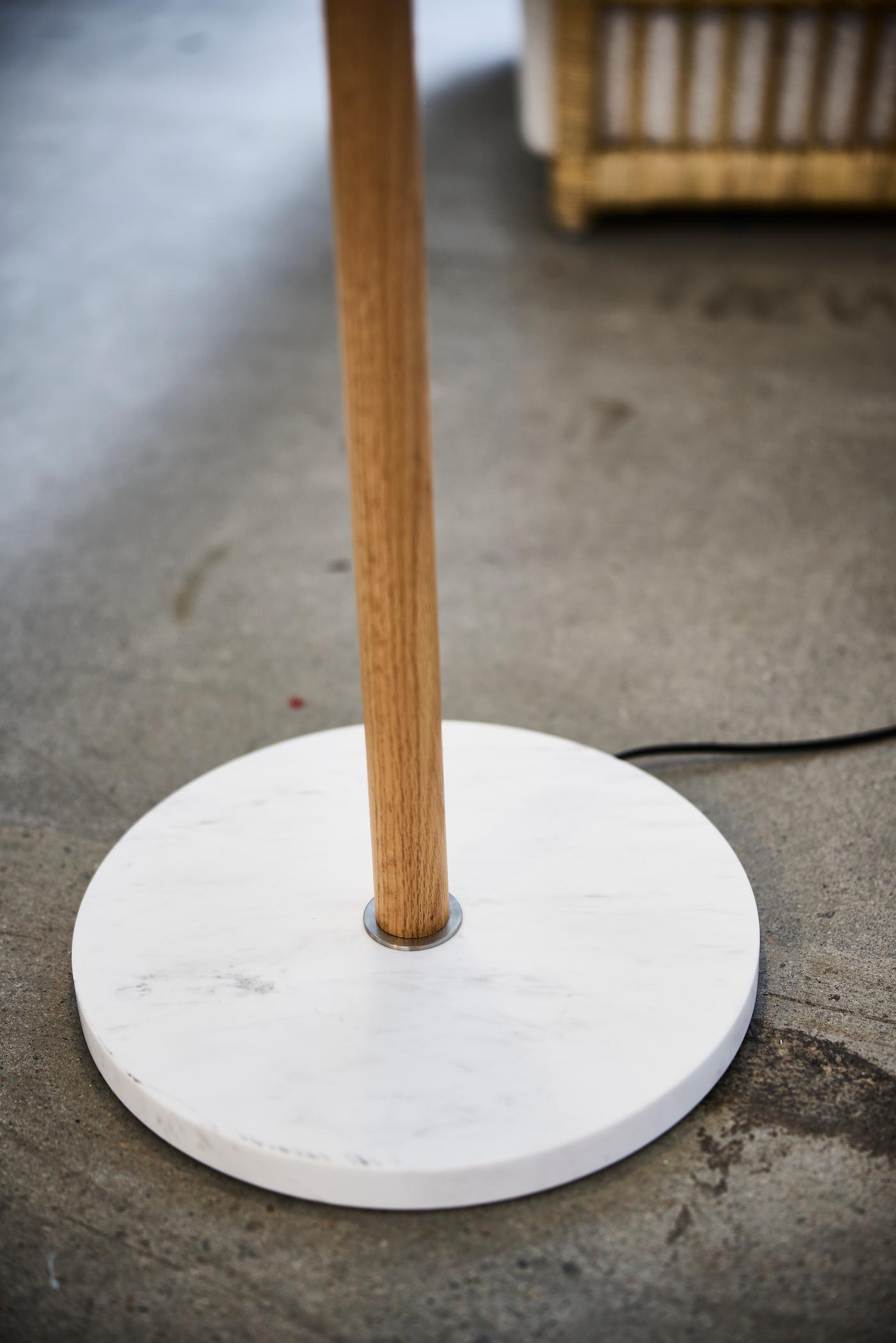 Close-up of wooden lamp stand fixed into a round white marble base on a concrete floor.