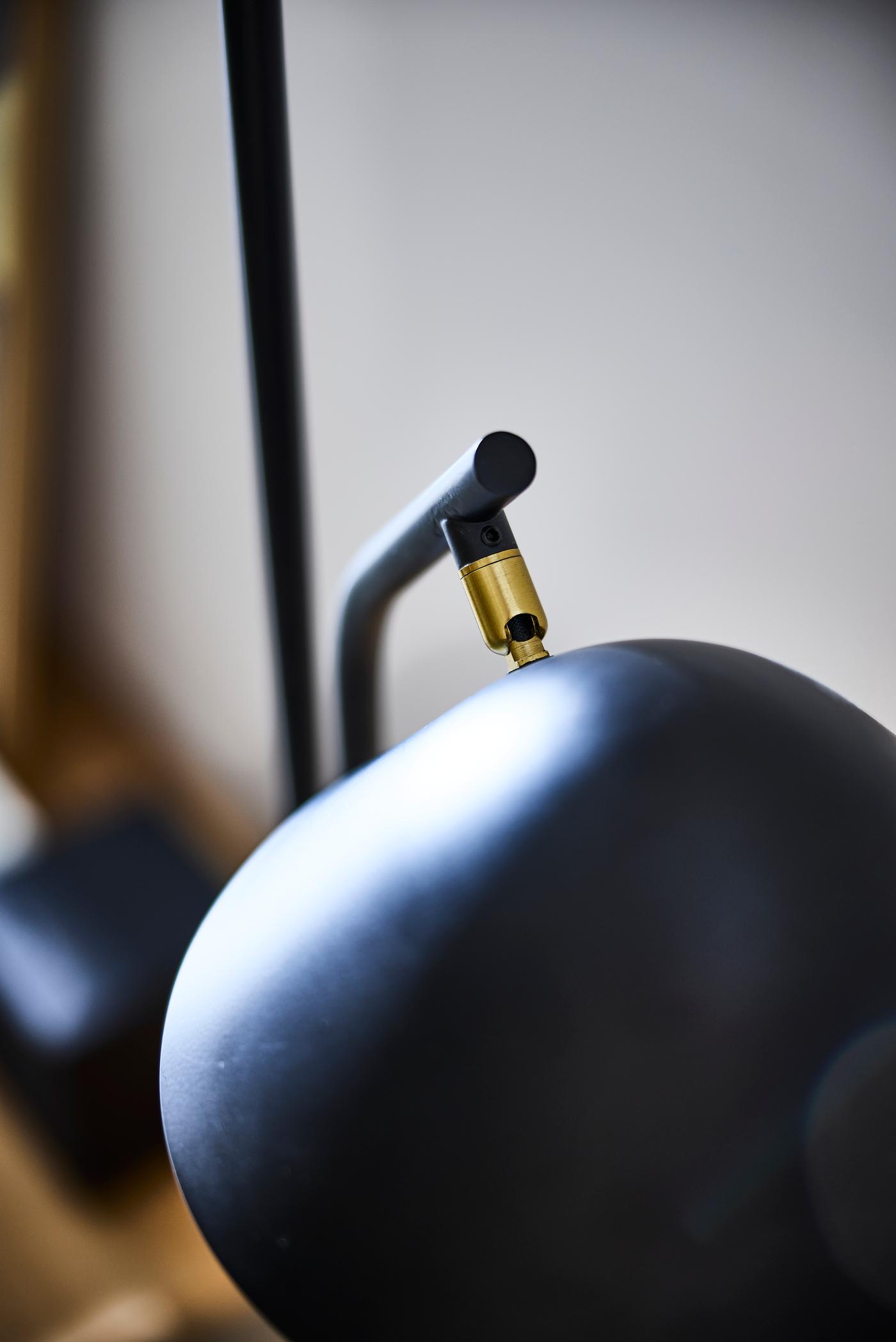 Close-up of black metal lamp head with brass joint, showing angled arm detail.