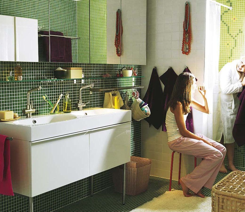 Two girls are in the bathroom. One is brushing her teeth, the other is drying her hair.