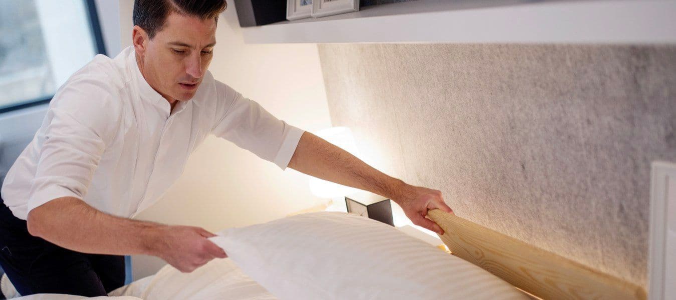 A man in a white shirt making a bed.