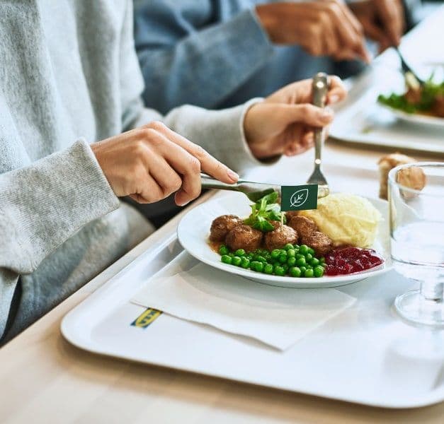 Two trays with meatballs, mashed potatoes, green peas and lingonberry jam. The hands of two customers cutting the food.