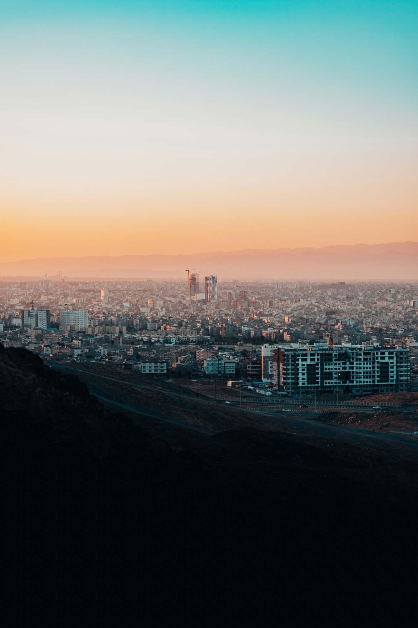 A dense cityscape during sunset. The view is from slightly afar, as if the city is in a valley.