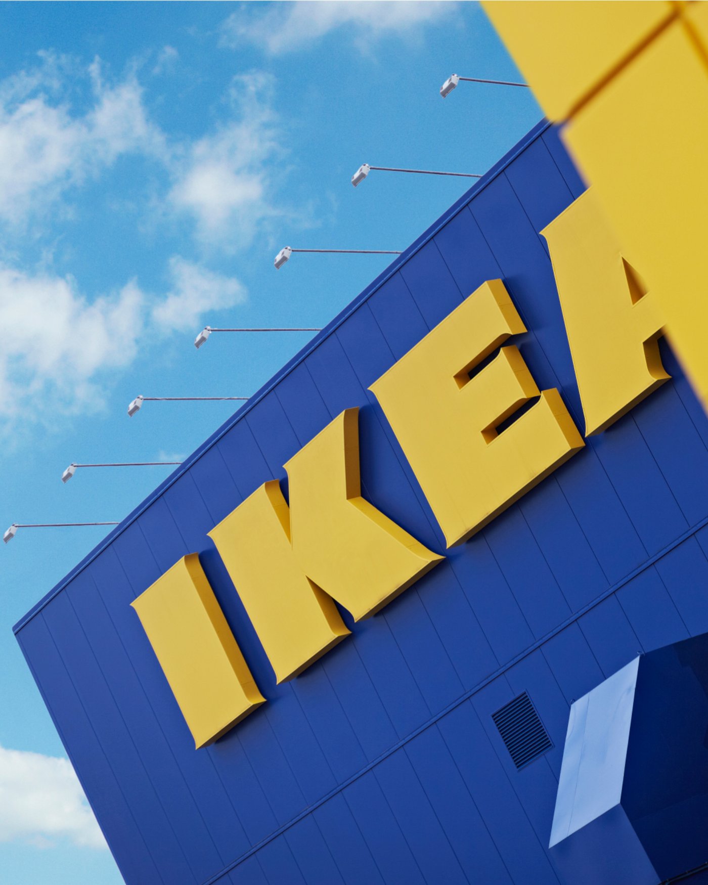 Close-up view of the yellow IKEA trademark on a blue store building under a bright sky with clouds