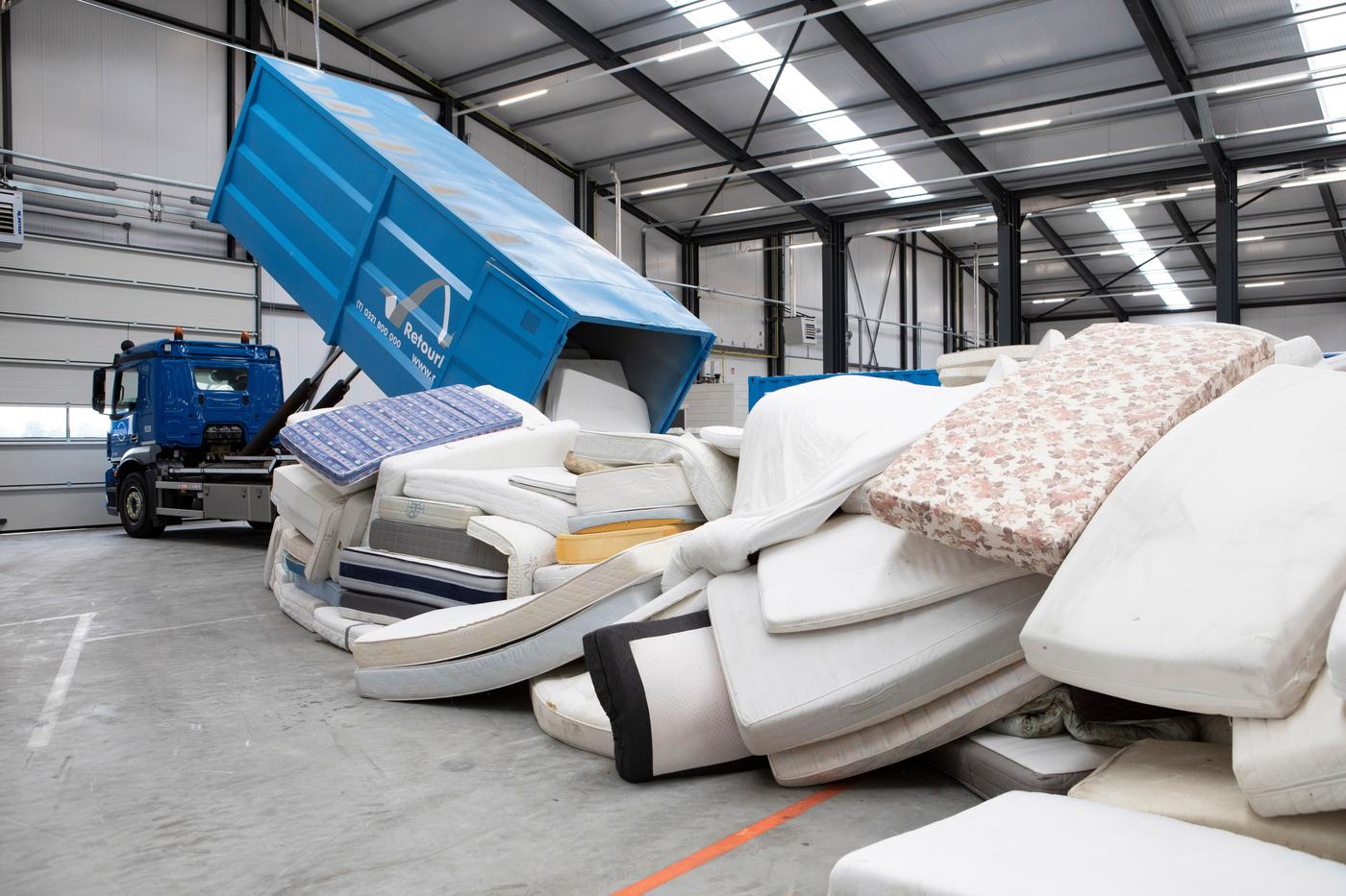 A truck unloading used mattresses on a factory floor.