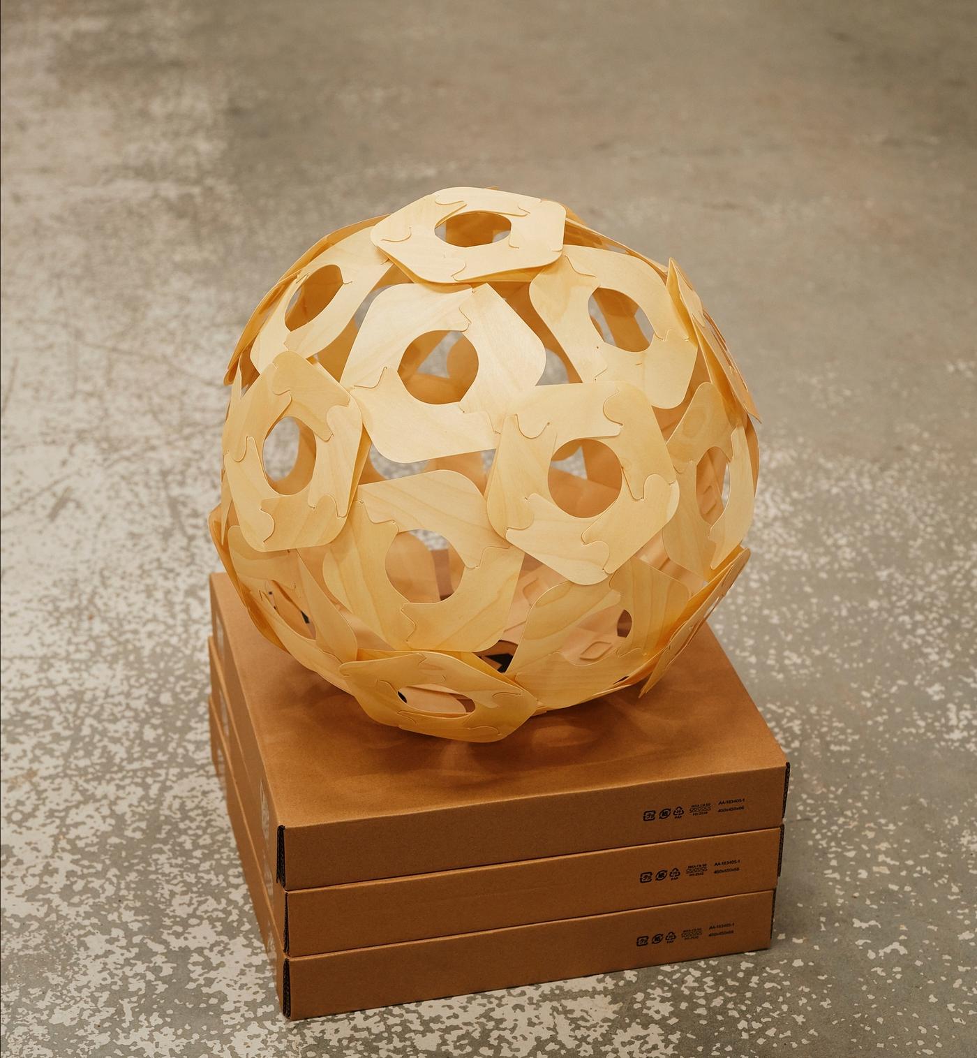 ÖDLEBLAD lamp shade resting on a stack of three of its own flatpack boxes.