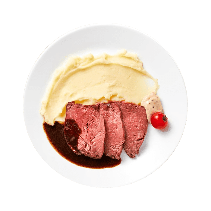 A plate of roast beef, mashed potato, gravy and a tomato.