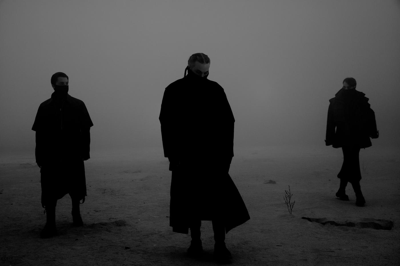 In a dimly lit grey space, the silhouettes of three people standing.