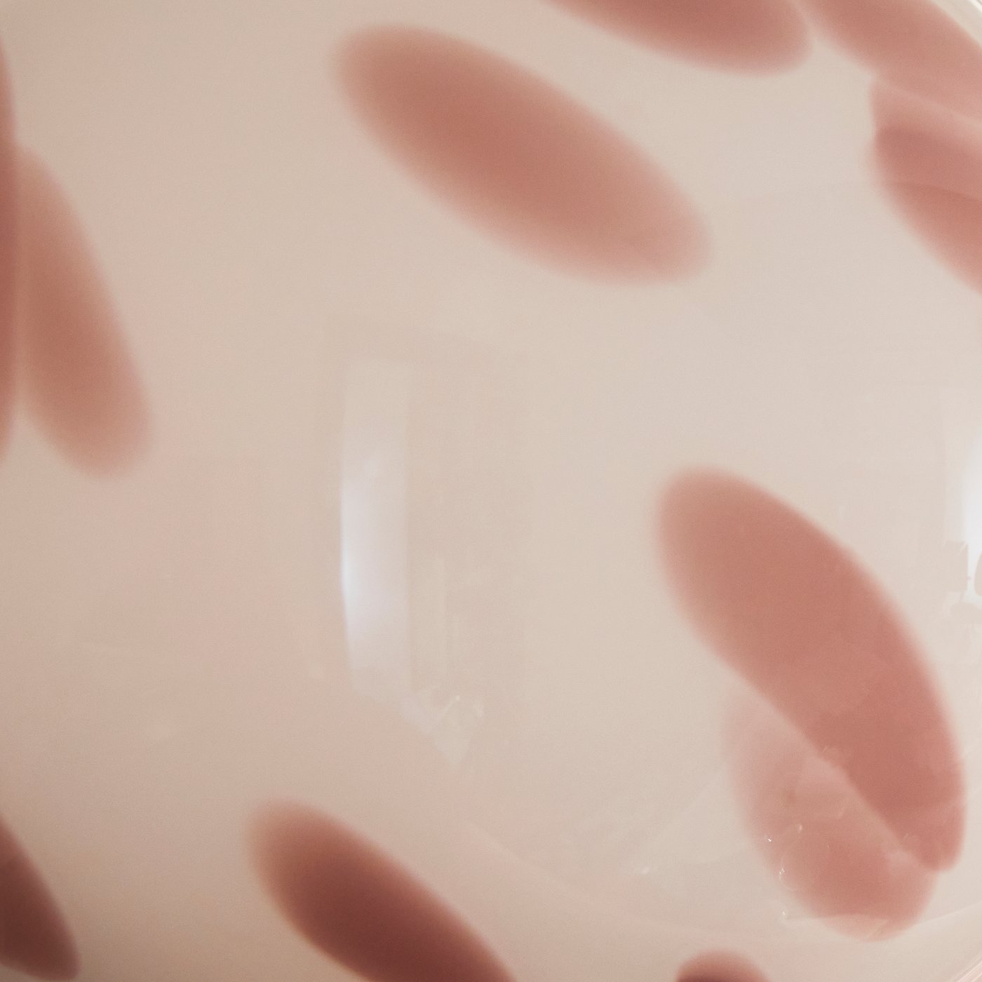 A close-up of a glass shade in white with pink blobs.