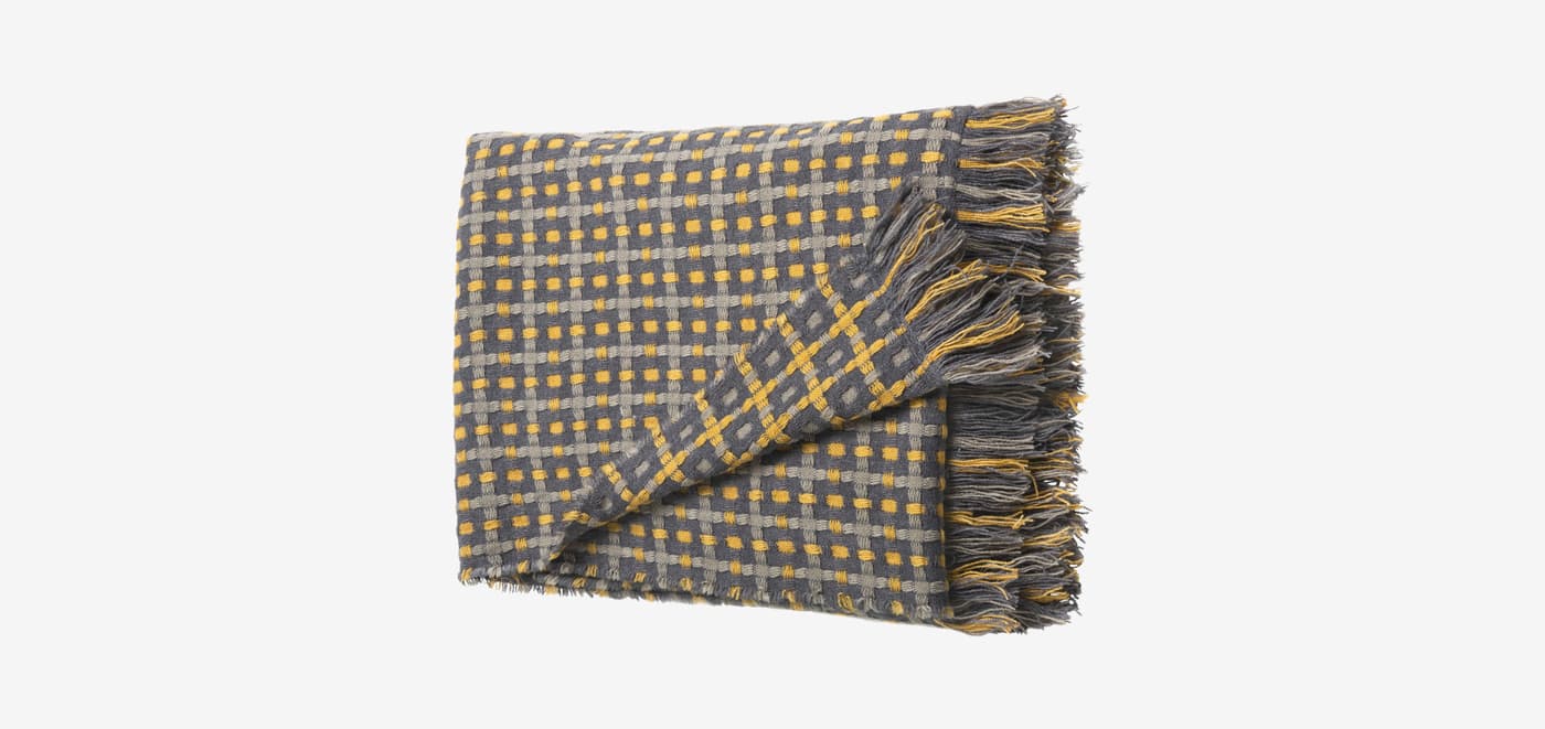 A grey and yellow FLIKBRUNÖRT throw with tassles.