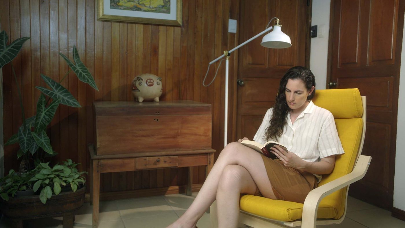 A person is sitting and reading in a yellow chair in a wood panelled living room. Next to the chair is a tall white reading lamp.